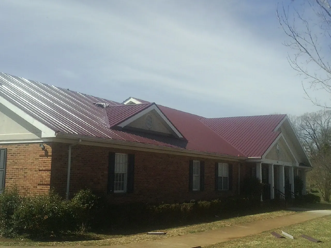 Red metal roof with gabled entries on a long brick building, from a Hail Damage Roof Repair job in Entiat