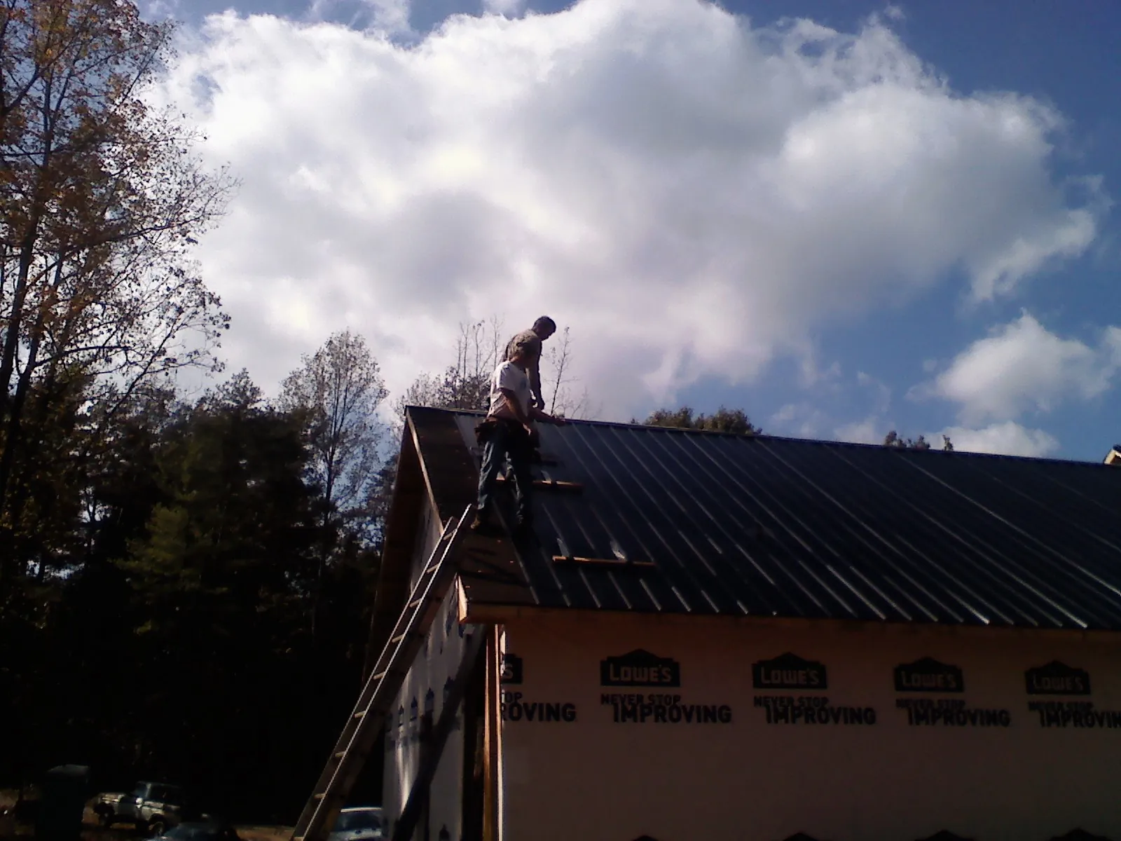 Roofer fastening dark metal panels high against a cloudy sky, from a Roof Inspection job in Entiat